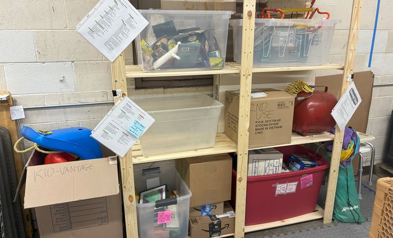 Wooden shelf with clear tubs, boxes, and red tubs filled with donations. 