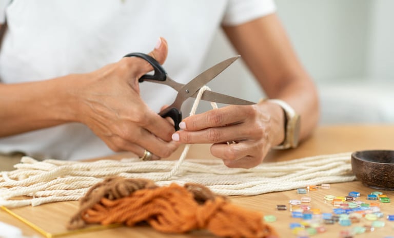 Una persona utilizando tijeras para cortar cordón de algodón blanco para un proyecto artesanal.