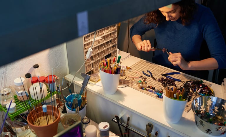 Artesana de joyería utilizando pinzas para crear joería hecha a mano con cuentas, en un escritorio