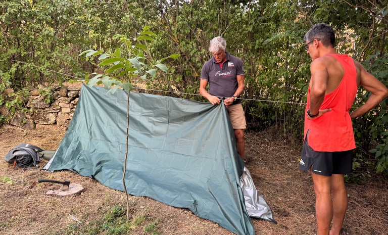 dos personas construyendo un refugio de fortuna con un tarp suspendido de una linea de cordino