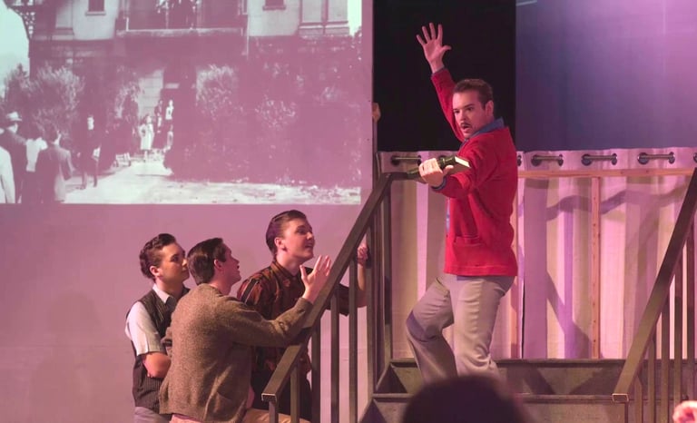 A male college student stands on the stairs in a frozen pose as an admirer sings about him.