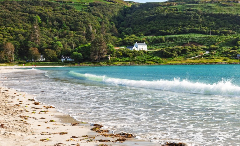 a beach with a house and a green hills