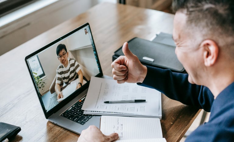 Two men having a virtual meeting on a laptop. One man is giving a thumbs-up.
