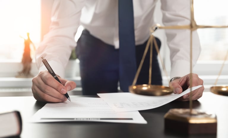 Person Signing Document in front of Scales of Justice