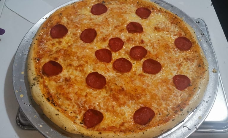 Pizza de pepperoni recién horneada con queso mozzarella fundido, sobre una bandeja redonda de metal.