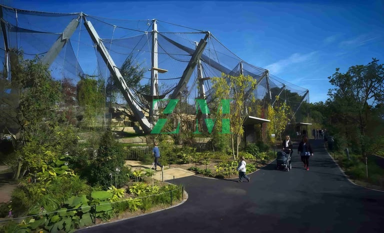 Visitors walk past the modern mesh Snowden Aviary at the London Zoo under a clear blue sky.