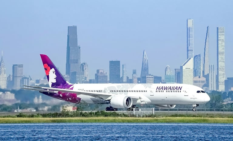 Hawaiian Airlines jet parked on a tarmac beside blue water and the city skyline in the background