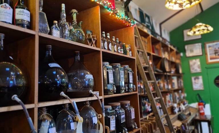 Wooden shelves in a rustic shop display glass wine carboys and assorted vintage liquor bottles.
