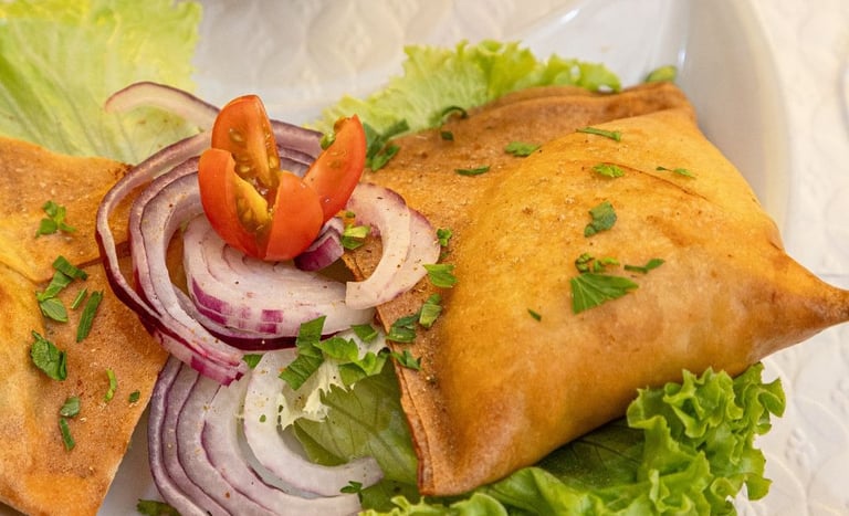 Golden fried vegetable samosas served on a plate with fresh lettuce, red onions, and cherry tomatoes.