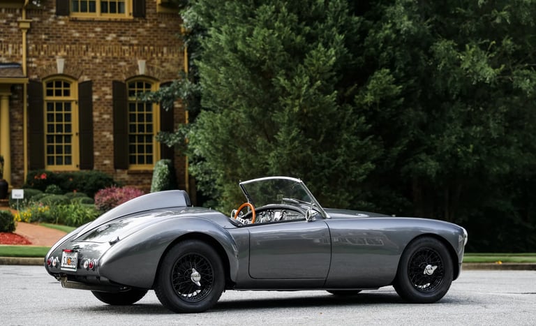 A side profile shot of a silver and black 1958 MG MGA Roadster in an elegant English courtyard
