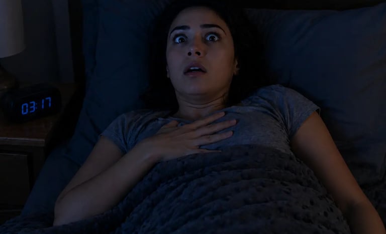 A startled woman waking up with a shocked expression in a dark bedroom at night.