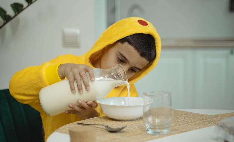 Bambino versa il latte in una ciotola durante la colazione
