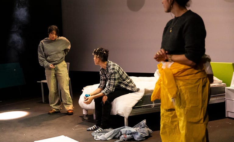 Two brown-skinned people in deep conversation, watched by a third person wearing a hazmat suit