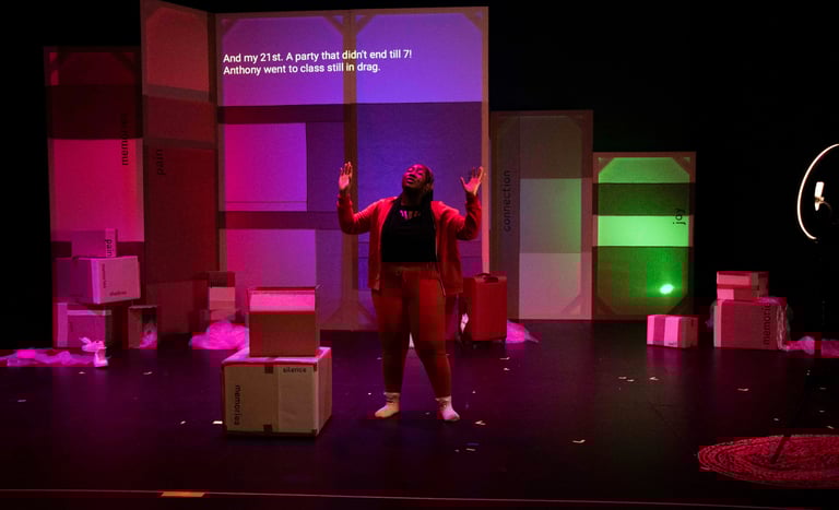 A black woman in front of rainbow lit boxes raises her arms to the ceiling