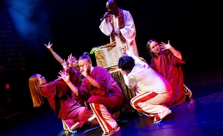 A black person in white robes, with a group of people in red and white at their feet