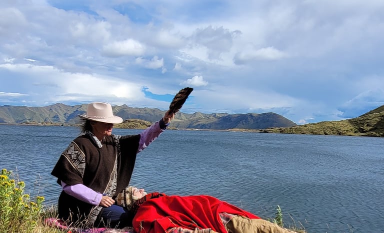 A shaman performs a spiritual healing ritual with a feather fan by a scenic mountain lake.