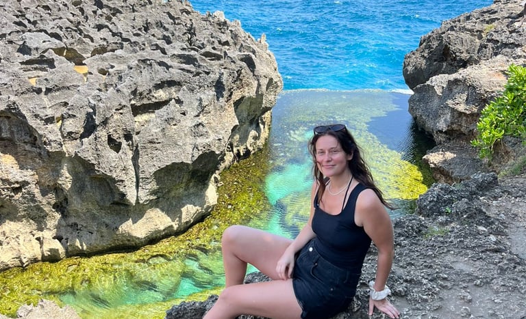 A woman sits on volcanic rocks by the turquoise waters of Angel's Billabong in Nusa Penida, Bali.