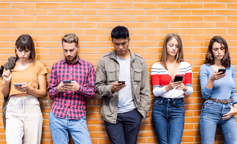 Teenagers leaning against a wall, fiddling with their smartphones.