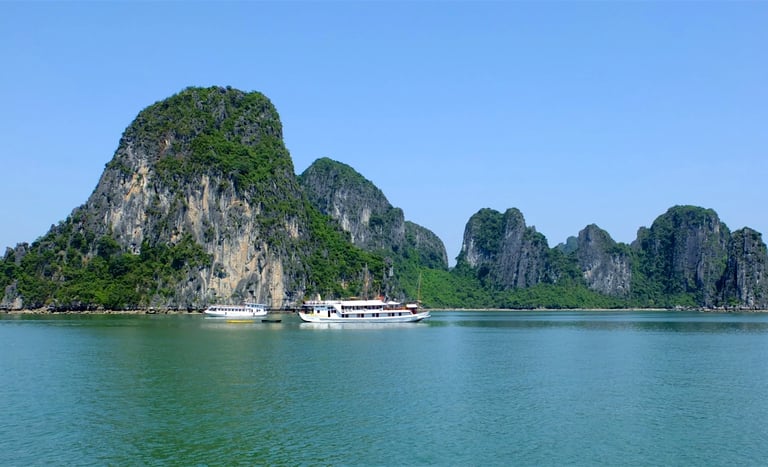 White cruise boats sailing past the iconic limestone karst mountains in Ha Long Bay, Vietnam.