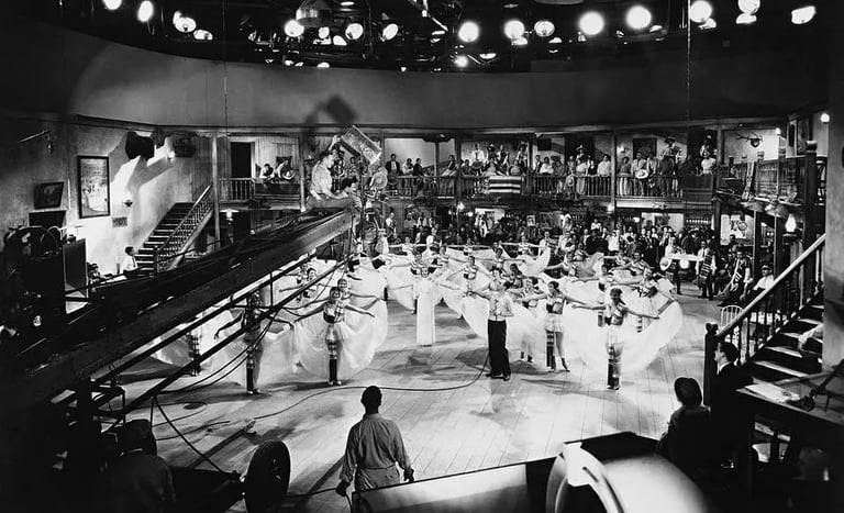 Berkeley perched on a crane with camera crew filming dancers holding skirts in symmetrical patterns.