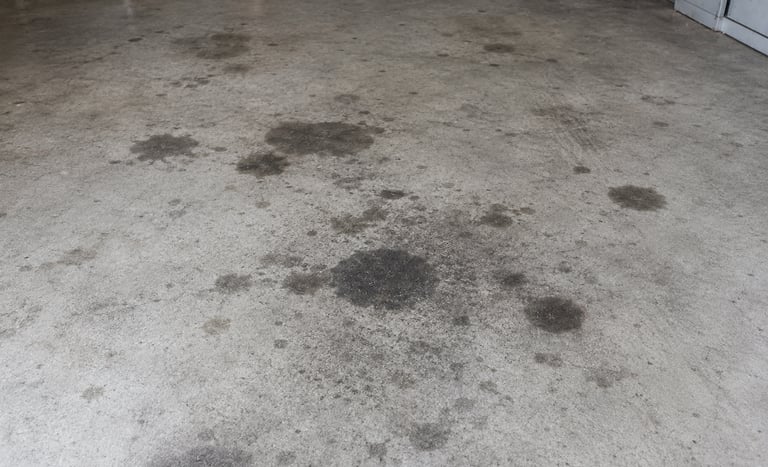 Dark oil stains and grease spots on a concrete garage floor near automotive tools.