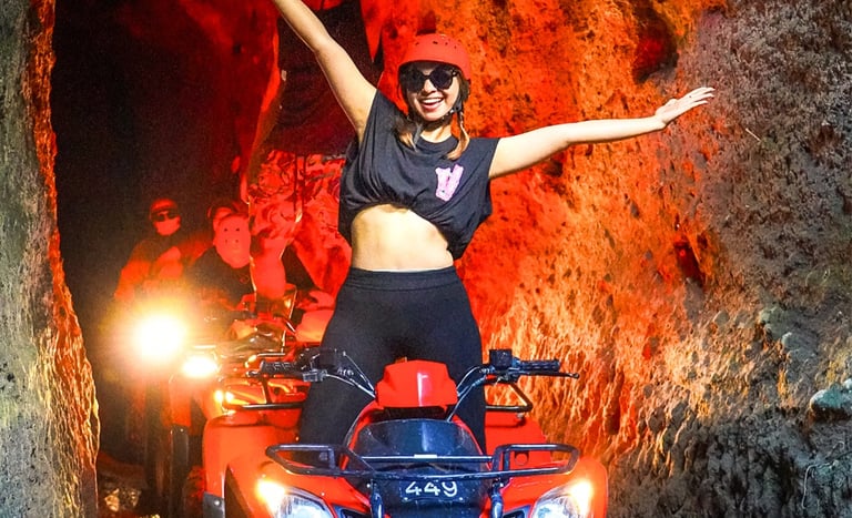 Excited tourists riding red ATV quad bikes through a narrow rock tunnel cave in Bali.