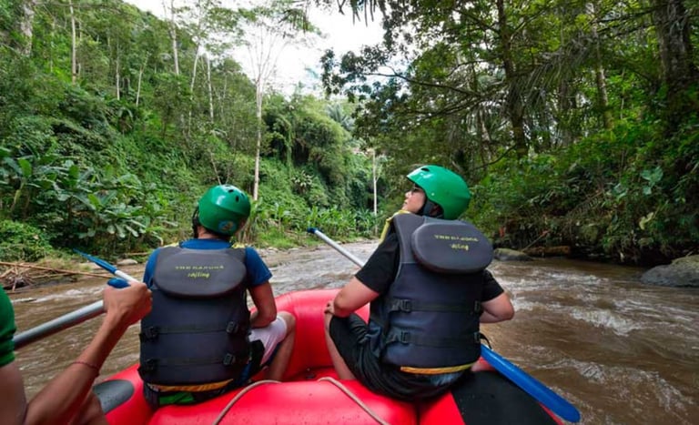 Two people wearing helmets and life jackets white water rafting down a river in a lush Bali jungle.