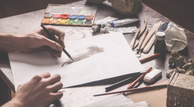 Photo of an artist working at a desk covered in art supplies