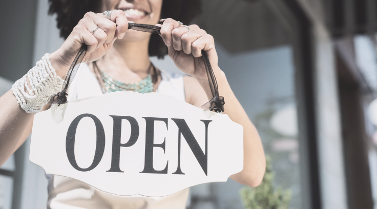 Photo of a small business owner smiling while holding an "open" sign