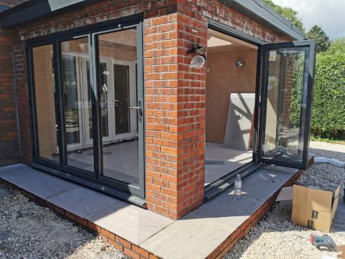 Modern anthracite grey bi-fold doors installed on a red brick home extension with stone patio.