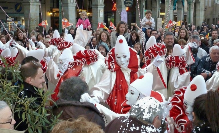 Crowd celebrates the Carnival of Limoux with performers in traditional red and white Pierrot costumes.