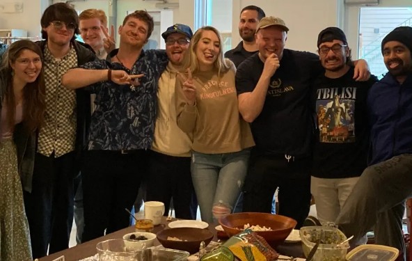 A diverse group of smiling friends posing together behind a table of party snacks and appetizers.