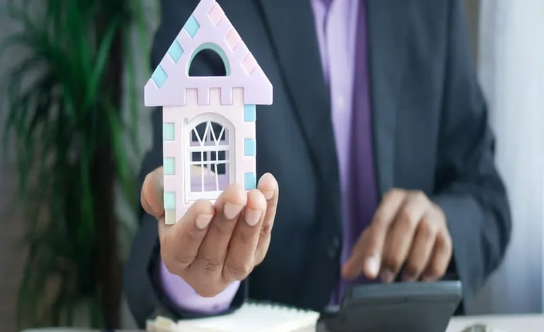 Real estate professional holding a small house model while doing calculations.