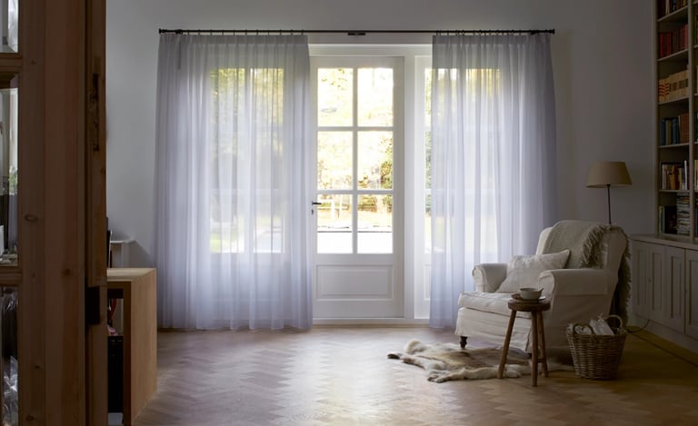 Grands rideaux tamisants blanc devant de larges fenêtres dans une entrée avec fauteuil et tapis