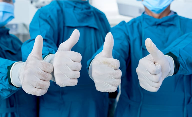 four physicians in gowns and gloves giving the thumbs-up approval sign.