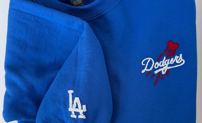 Folded royal blue Los Angeles Dodgers sweatshirt with embroidered team logo and heart detail.