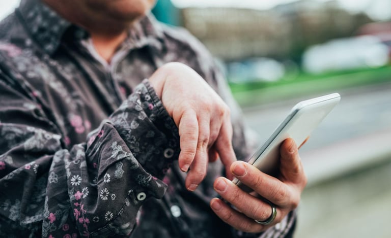 A person in a patterned shirt uses a smartphone outdoors