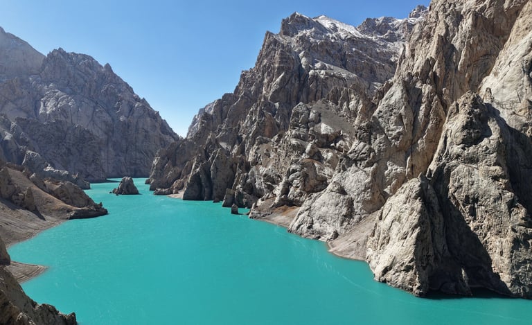 Turquoise alpine lake surrounded by steep, rocky mountain peaks under a clear blue sky.