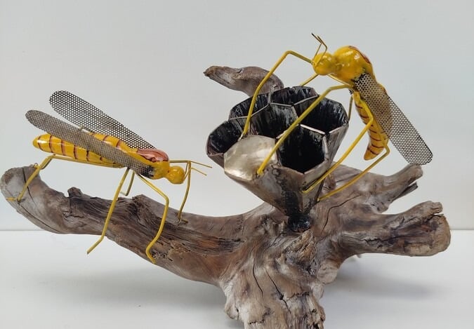 Handmade metal yellow jackets sculpture on driftwood base with a honeycomb nest.
