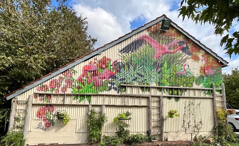 une grange en taule et une fresque avec des flamands roses et des plantes