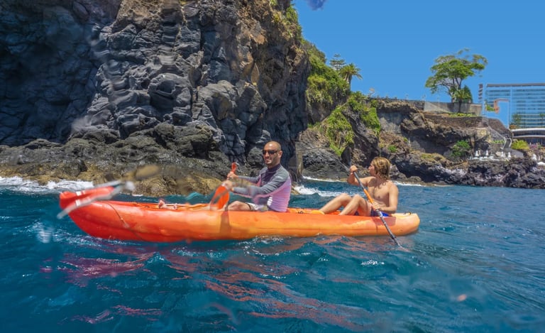 Guide and guest paddling an orange tandem kayak along the rocky volcanic cliffs of Funchal, Madeira