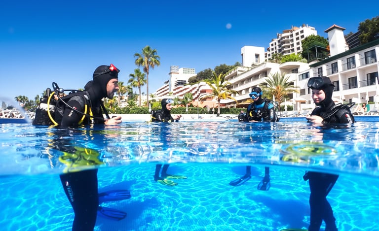 Scuba divers training in a clear blue Funchal resort pool, Madeira Island, under a sunny sky with coastal architecture.