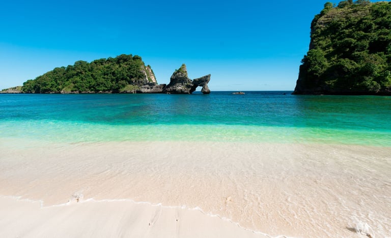 two women walking into turquoise ocean on a white sandy beach with limestone cliffs and lush green islands under blue sky