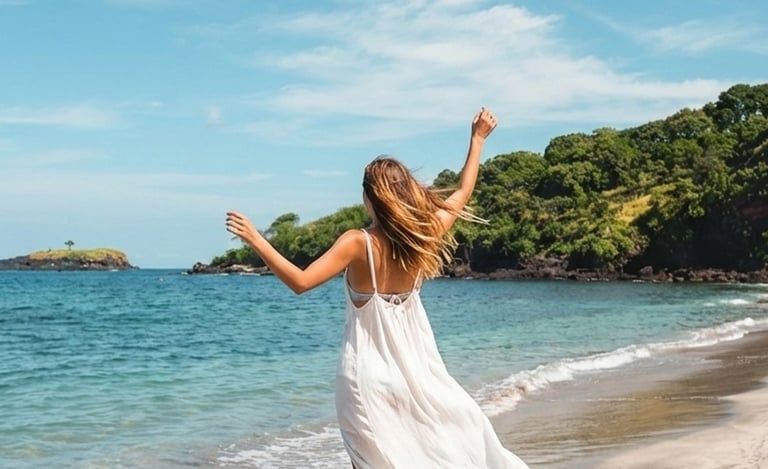 A woman in a flowing white dress stands barefoot on the sandy shore of Virgin Beach, Karangasem, Bali, facing the turquoise s