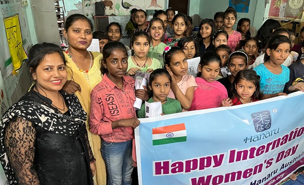 Group of twenty girls, some holding up an International Women's Day banner
