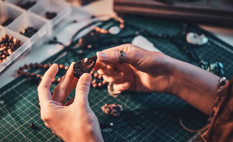 Manos sosteniendo una piedra natural en mesa de trabajo de joyería artesanal.