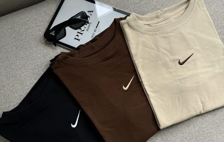 Tres sudaderas Nike de cuello redondo dobladas en colores neutros.