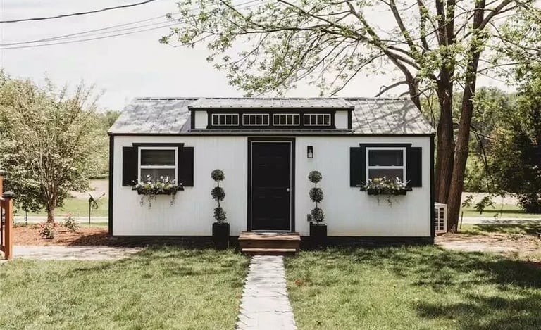 Custom she shed with white LP SmartSide® siding, black trim, and flower boxes in a landscaped yard