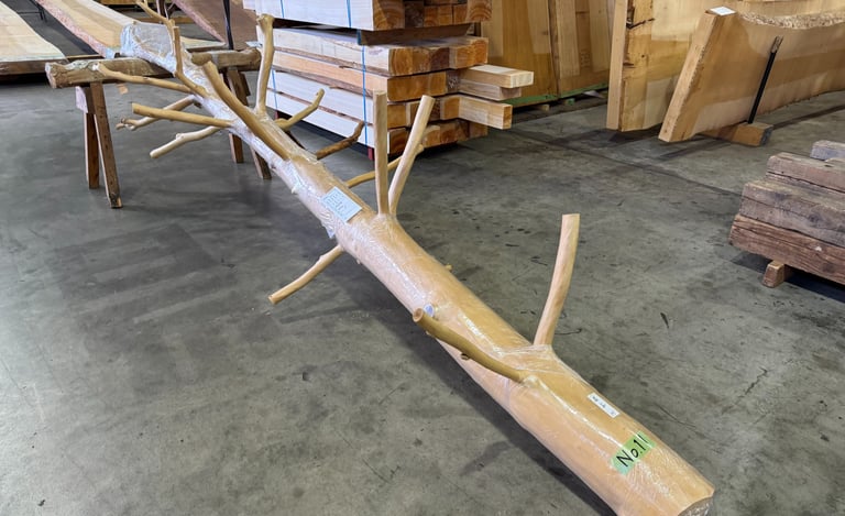 A raw, de-barked log with natural branches for woodworking inside a lumber warehouse.