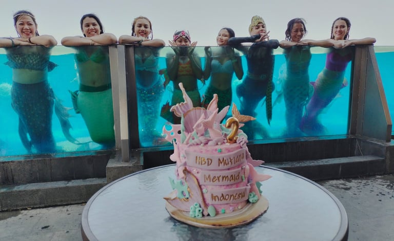 a birthday cake in ocean mermaid theme and the celebrating mermaids in the background, swimming in a